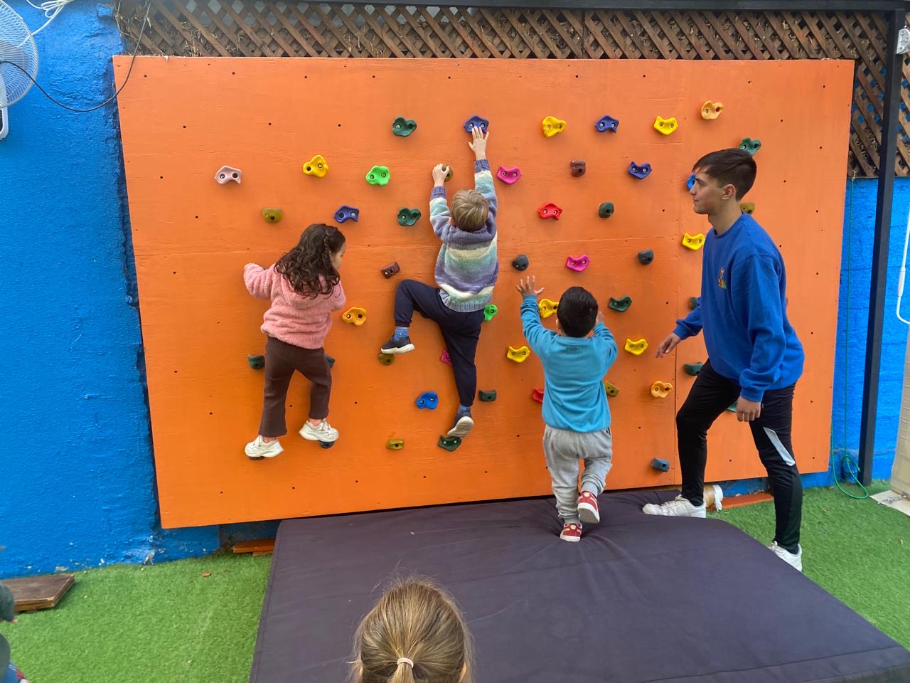 Niños escalando el muro de escalada con acompañamiento docente